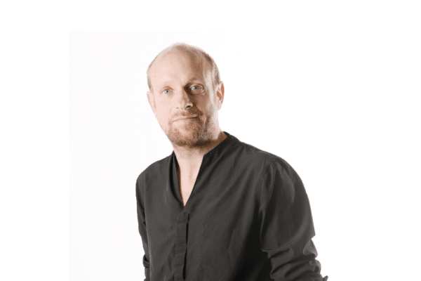 Homme debout en chemise noire, fond blanc.